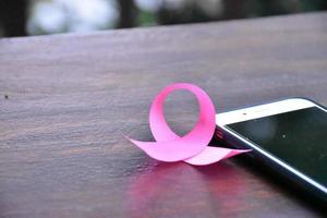 Pink ribbon on table with mobile phone. Concept for protesting and supporting the breast cancer against in woman. photo