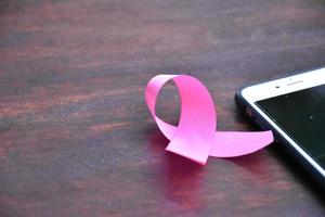 Pink ribbon on table with mobile phone. Concept for protesting and supporting the breast cancer against in woman. photo