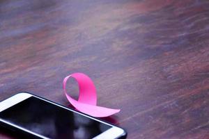 Pink ribbon on table with mobile phone. Concept for protesting and supporting the breast cancer against in woman. photo