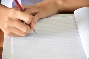 Front view of Asian student holding a pen in hand and doing the test in classroon. Concept for testing, writing and doing assignment and homework. Selective focus on hand and pen. photo