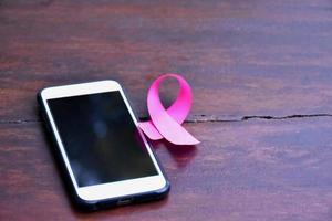 Pink ribbon on table with mobile phone. Concept for protesting and supporting the breast cancer against in woman. photo