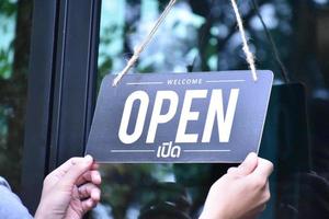 el dueño de la tienda está colgando la etiqueta 'abierta' en las ventanas de vidrio para abrir la tienda y dar la bienvenida a los clientes. El idioma tailandés en la imagen significa 'abierto' en inglés. foto