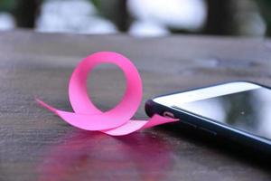 Pink ribbon on table with mobile phone. Concept for protesting and supporting the breast cancer against in woman. photo