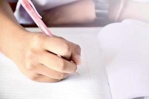 vista frontal de un estudiante asiático sosteniendo un bolígrafo en la mano y haciendo la prueba en clase. concepto para probar, escribir y hacer tareas y tareas. enfoque selectivo en la mano y la pluma. foto