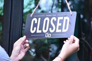 Shop owner is hanging 'Closed' label on glass windows to open the shop and welcome customers. Thai language in the picture means 'Open' in English. photo