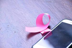 Pink ribbon on table with mobile phone. Concept for protesting and supporting the breast cancer against in woman. photo