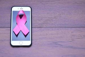 Pink ribbon on table with mobile phone. Concept for protesting and supporting the breast cancer against in woman. photo