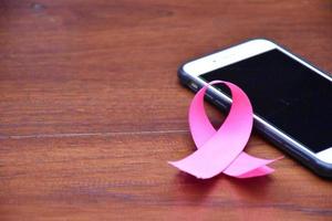 Pink ribbon on table with mobile phone. Concept for protesting and supporting the breast cancer against in woman. photo