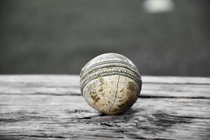 antiguos equipos deportivos de cricket de entrenamiento en suelo oscuro, pelota de cuero, wickets, casco y bate de madera, enfoque suave y selectivo, concepto tradicional de amantes del deporte de cricket en todo el mundo. foto