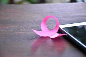 Pink ribbon on table with mobile phone. Concept for protesting and supporting the breast cancer against in woman. photo