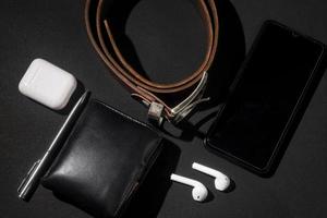 set of men's stuff on black background. smartphone, wireless earphone, leather belt, leather wallet and ballpoint pen photo