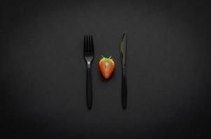 Cortar fresa con tenedor y cuchillo sobre fondo oscuro para un concepto minimalista de comida negra plana. foto
