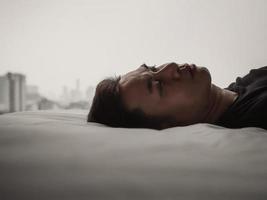 Asian man feels sad alone on bed with city background. Stay home, depression and loneliness concept. photo