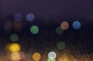 Rain drop on glass window in monsoon season with colorful bokeh lights for abstract and background concept. photo