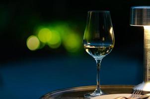 A glass of white wine on table at night with green bokeh background from garden. photo