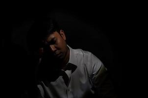 Asian miserable depressed man sitting alone in dark background. Depression and mental health concept. photo