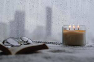 Burning aroma candle puts near by window that have rain drop in monsoon season photo