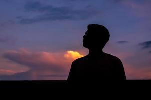 Silhouette of asian man stay alone with dusk sky background. Depression and mental health concept. photo