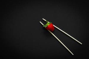 Strawberry and chopsticks on dark background for minimalist flat lay black food concept. photo