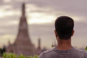 A tourist holding a glass of white wine looking at blurred background of temple. photo