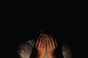 Asian miserable depressed man sitting alone in dark background. Depression and mental health concept. photo