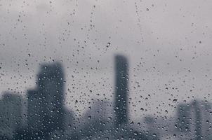 Rain drop on glass window in monsoon season with blurred city buildings background.