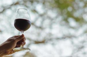 Hand toasting a glass of red wine blurry green background. photo