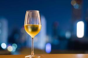 A glass of white wine puts on table at balcony with blurred city background. Relaxing at home concept. photo