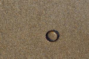 una tapa de refresco con óxido en la arena limpia y húmeda de la playa con sombra de la luz del sol. foto