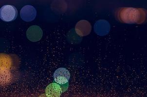 Rain drop on glass window in monsoon season with colorful bokeh lights for abstract and background concept. photo