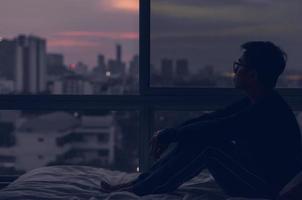 el hombre sentado en la cama con vista a la ciudad desde el dormitorio. foto