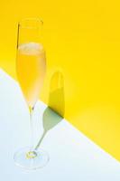 A glass of cold Champagne with vapour that has shadow from sun light on blue and yellow background. Summer concept. photo