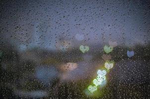 gota de lluvia en la ventana con coloridas luces de forma de amor bokeh. foto