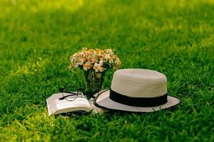 ocio en el jardín con libro, sombrero de paja y flores en el césped. foto