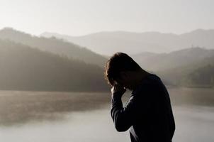 un hombre asiático miserable y deprimido está solo con el fondo de la montaña y el lago. concepto de depresión y salud mental. foto