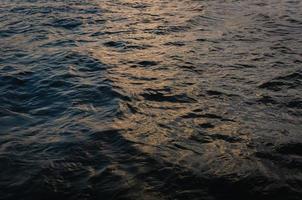 superficie de onda del río azul oscuro con luz solar sobre el agua cuando se pone el fondo. foto