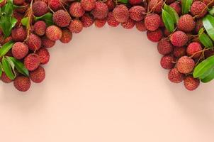 Fresh lychee fruits with leaves on beige color background. Top view, frame and background concept. photo