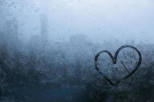 Heart painted on window which fogged up with blurred city background. photo