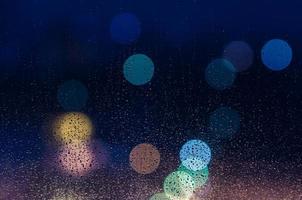 Rain drop on glass window in monsoon season with colorful bokeh lights for abstract and background concept. photo