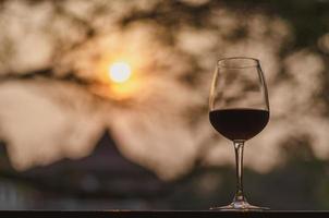 una copa de vino tinto en la mesa con fondo de puesta de sol. foto