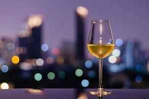 A glass of white wine on table of rooftop bar with colorful city bokeh lights. photo