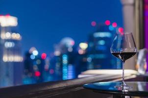 una copa de vino tinto en la mesa del bar de la azotea con un colorido bokeh de luces de la ciudad. foto