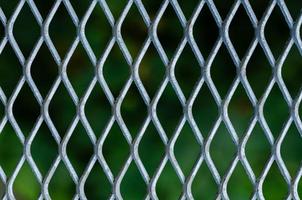 Silver grid of metal fence with blurred green color background. photo