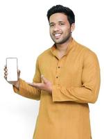 retrato de un joven alegre que usa kurta en un fondo aislado, mostrando un teléfono móvil de pantalla en blanco. foto