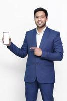 Young businessman in suit, holding blank screen smartphone and pointing to it, copy space for advertising on isolated background. photo