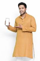 Portrait of a cheerful young man wearing kurta on isolated background, showing blank screen mobile phone. photo