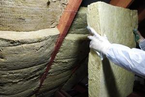 un hombre con un mono protector pone lana mineral entre la viga del techo de la casa para calentarse del frío foto