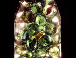 Close-up shot of glass marbles inside a bottle with a dark background. Diversity of marbles color photo