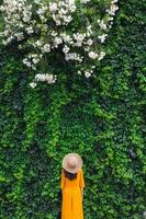 A girl in a straw hat stands near a wall overgrown with ivy photo