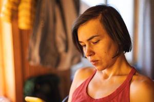 a woman sits near the window and holds a smartphone photo